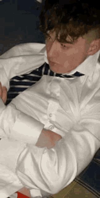 a young man in a white shirt and tie is laying on the floor .