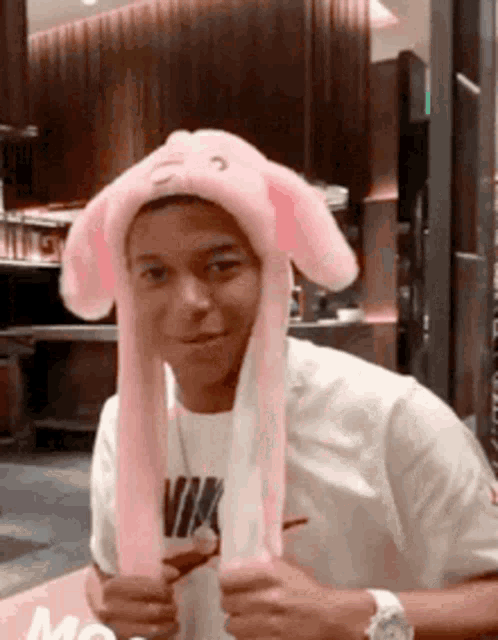 a young man wearing a pink bunny hat is smiling for the camera .
