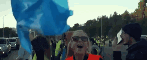 a woman wearing sunglasses holds a blue flag in front of a crowd of people