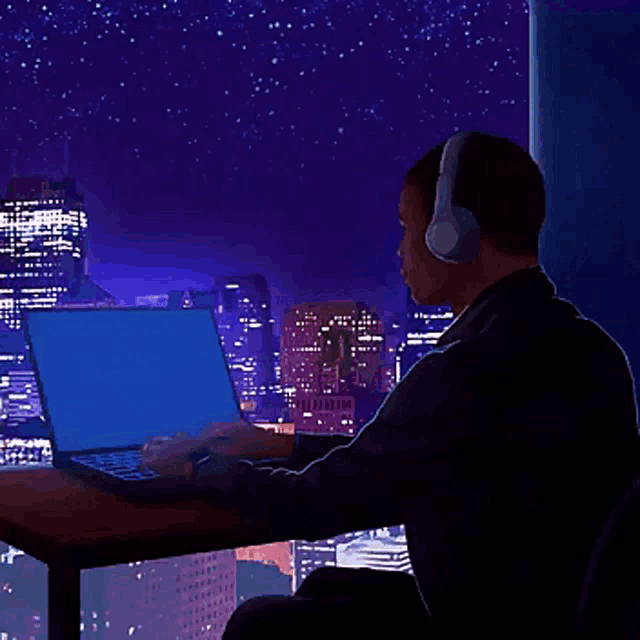 a man wearing headphones sits at a desk using a laptop
