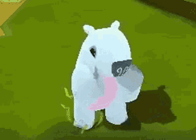 a white teddy bear with a pink stomach is standing on top of a green field .