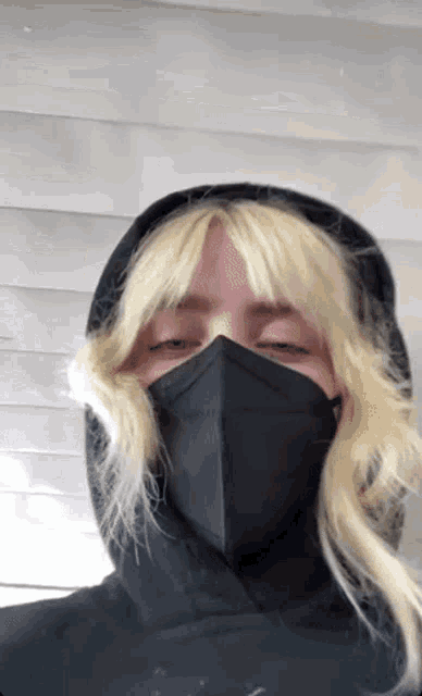 a woman with blonde hair wearing a black face mask and a black hoodie .