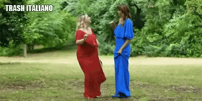 two women in red and blue dresses are dancing in a park with the text trash italiano above them .