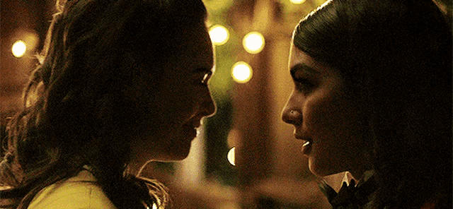 two women are looking at each other in a dark room with lights in the background