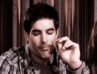 a man in a plaid shirt is sitting at a table with his eyes closed and holding something in his hand .