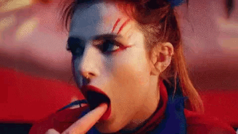 a woman with makeup on her face is licking her fingers .