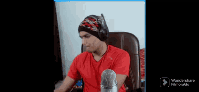 a man in a red shirt is sitting in front of a microphone and wondershare filmorago is visible