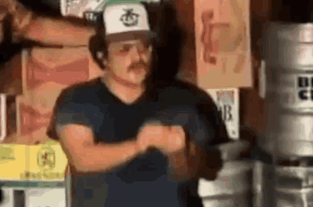 a man wearing a hat and a mustache is standing in a room with a bunch of beer kegs .