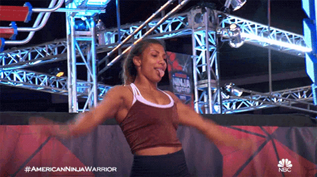 a woman is dancing in front of a sign that says american ninja warrior on it