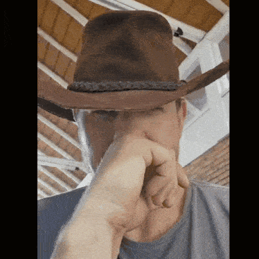 a man wearing a cowboy hat covering his nose