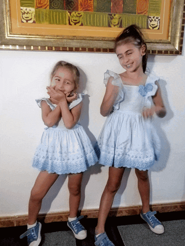 two little girls standing next to each other in front of a picture