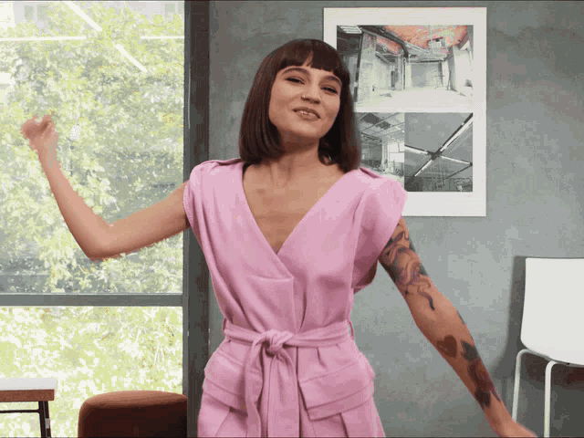 a woman in a pink dress is dancing in front of a window
