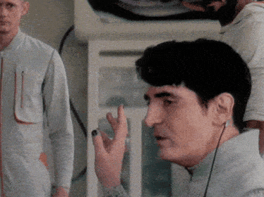 a man wearing ear buds talks into a microphone while another man looks on