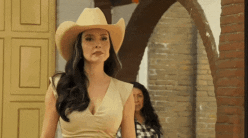 a woman wearing a cowboy hat is standing in front of a brick building