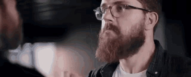 a bearded man wearing glasses is talking to another man .