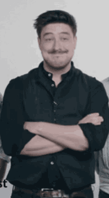 a man with a mustache is standing with his arms crossed in front of a white background