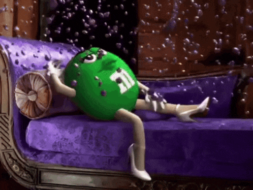 a green m & m laying on a purple couch surrounded by bubbles