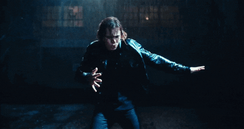 a man in a black leather jacket is pointing at something in the rain