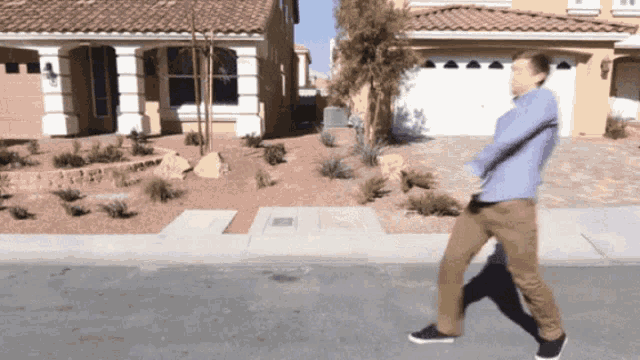 a man in a blue shirt is walking down a sidewalk in front of a house