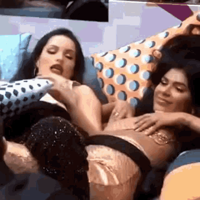 two women are laying on a couch with pillows and one is touching the other 's chest .
