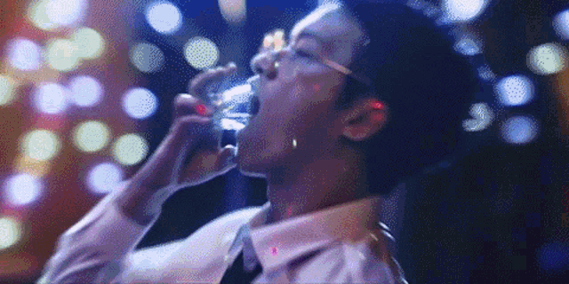 a man in a white shirt and tie is drinking a glass of water