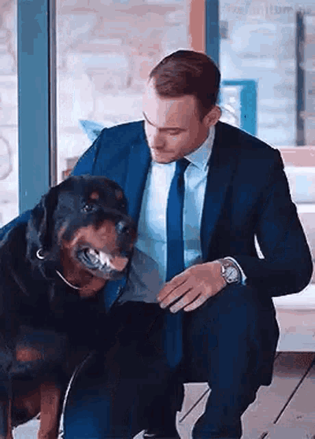 a man in a suit is kneeling down next to a dog .