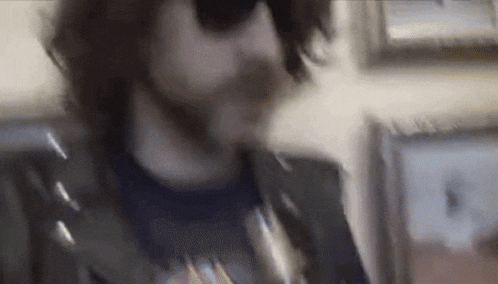 a man with a beard and sunglasses is eating a sandwich in a kitchen .