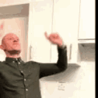 a man in a green shirt is giving a thumbs up in a kitchen