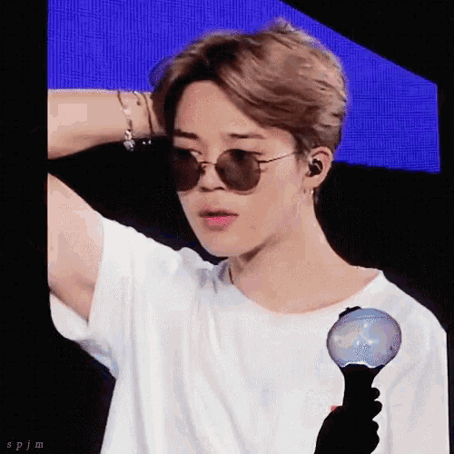 a young man wearing sunglasses and a white shirt is holding a light stick .