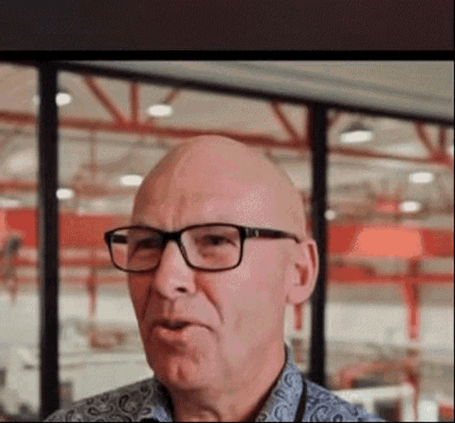 a bald man wearing glasses is talking in a room .