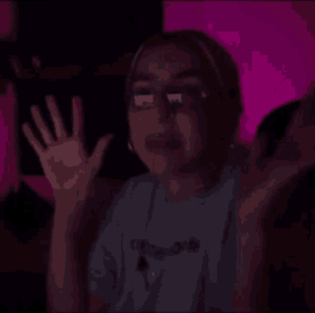 a woman wearing glasses is sitting in a dark room with her hands up .