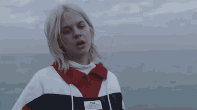 a woman wearing a fila sweatshirt stands in front of the ocean