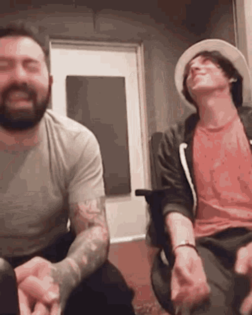 two men are sitting next to each other in a room laughing .