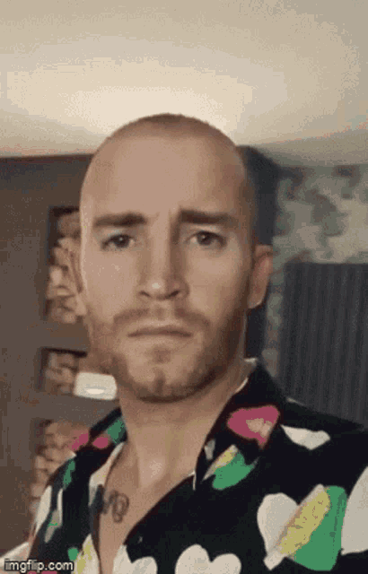a bald man with a beard is wearing a colorful shirt and making a face .