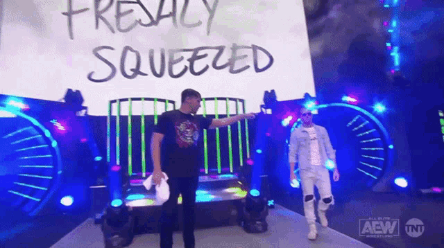 two men are standing in front of a sign that says ' freakly squeezed ' on it .
