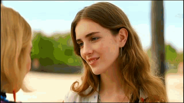 a close up of two women looking at each other with trees in the background
