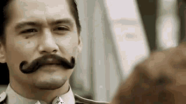 a man with a mustache is talking to another man in a suit .