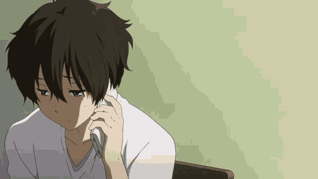 a boy with dark hair is sitting at a desk talking on a cell phone
