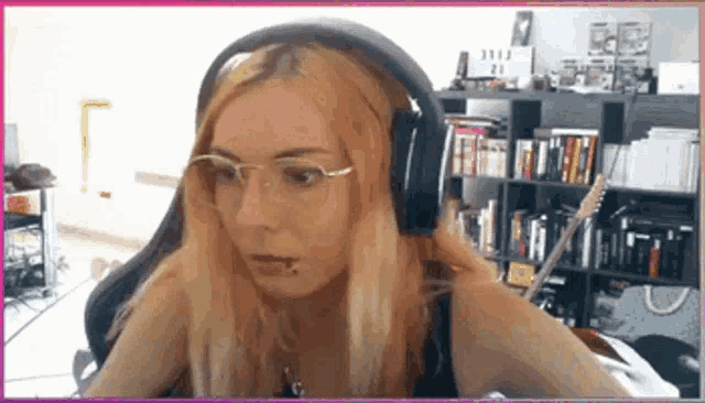 a woman wearing glasses and headphones is sitting in front of a bookshelf holding a guitar .