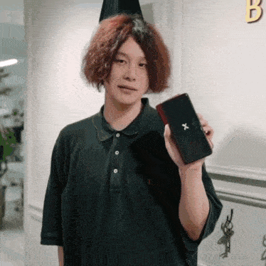 a man in a green polo shirt is holding a black phone with a x on it