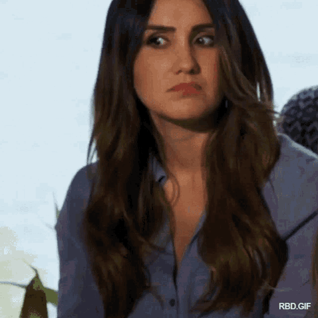 a woman with long hair is wearing a blue shirt and making a face .