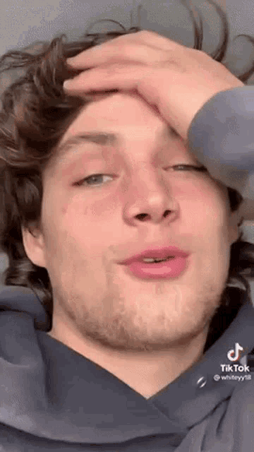 a young man with a beard is covering his face with his hand and making a funny face .