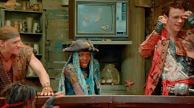 a group of people dressed in pirate costumes are standing around a table in front of a television .