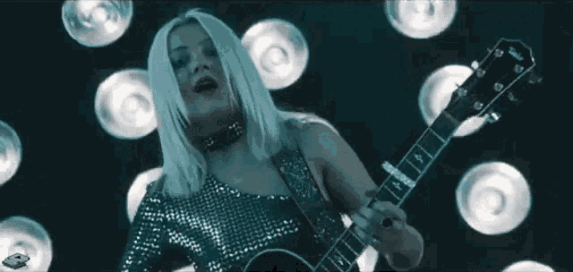 a woman is playing a guitar and singing into a microphone while surrounded by lights .