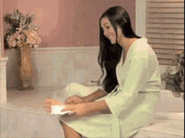 a woman in a bathrobe is sitting on the edge of a bathtub holding a piece of paper
