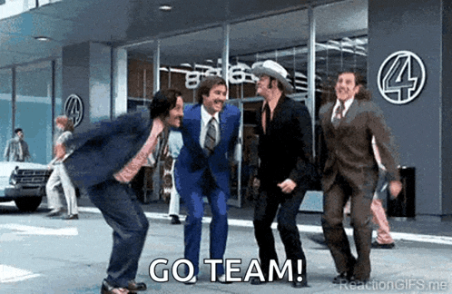 a group of men in suits and ties are dancing in front of a building with the words go team written on the bottom .