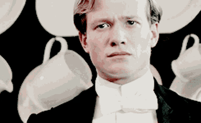 a man in a tuxedo and bow tie stands in front of a display of tea cups and saucers