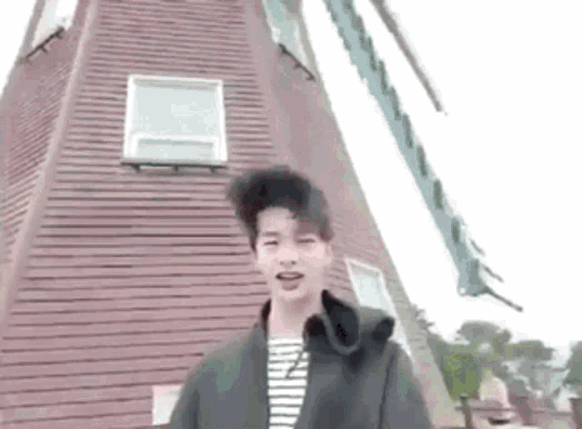 a young man is standing in front of a windmill in a park .