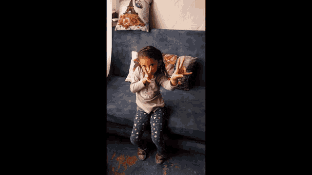 a little girl is sitting on a blue couch with a pillow that has the eiffel tower on it
