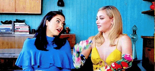 two women are sitting next to each other in a living room talking .